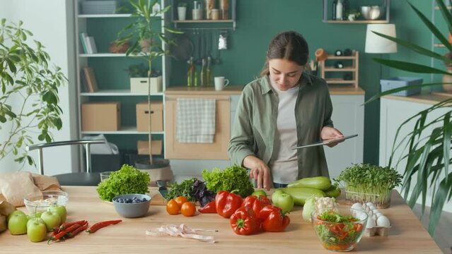 Young Woman Makes a Diet Plan of Correct Nutrition Using a Tablet in the Kitchen, Using a Calorie Counter in a Weight Loss App. Nutrition and Dietetics. Healthy Food and Technology Concept.