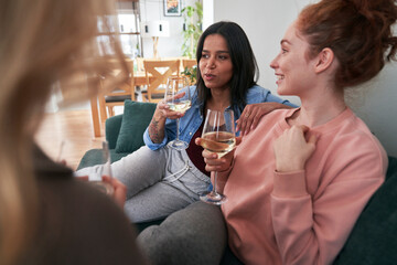 Three  female caucasian friends chatting and drinking wine at home