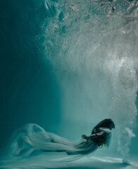 Beautiful woman in bridal dress swims and dives underwater with bubbles..