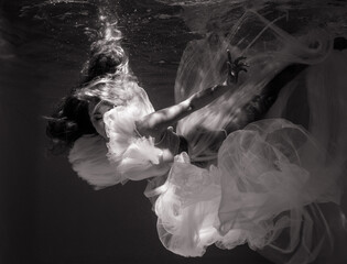 Beautiful woman in bridal dress swims and dives underwater.