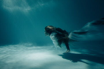 Obraz na płótnie Canvas Woman in bridal dress swims and dives underwater.