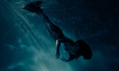 Woman with mermaid tail swims and dives underwater.
