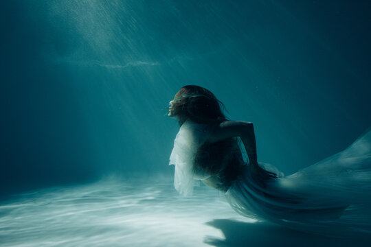 Woman in bridal dress swims and dives underwater.