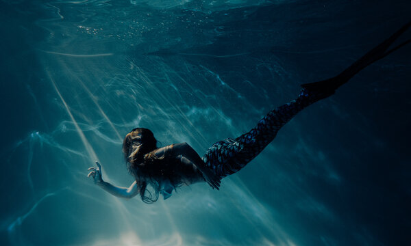 Woman with mermaid tail swims and dives underwater.