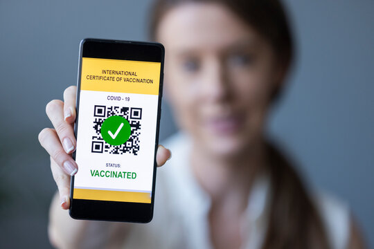 Defocused young woman showing smartphone with valid digital international vaccination certificate for COVID-19. Focus is on the smart phone.