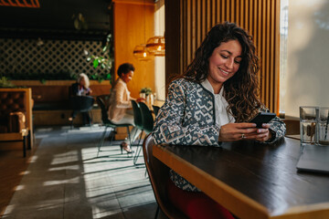 Young adult woman sitting at cafe and using phone