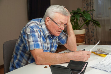 Upset depressed Senior man sitting at the table and calculating finances. Old man checking bills....