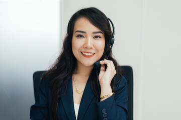 Portrait of Asian female telemarketer talking to customer at desk in the office looking at camera....