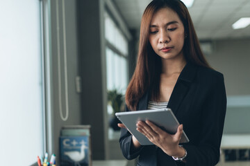 Fototapeta premium Asian female employee working on digital tablet in the office. checking and preparing for work