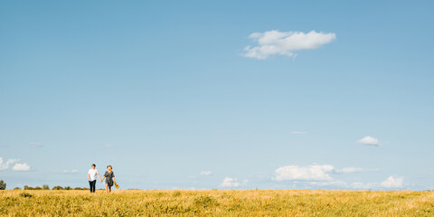 Caucasian love couple holding hands walking on horizon in nature on sunny summer day, young family against blue sky, distant look. Copy space banner. Romantic trip, love story adventure concept.