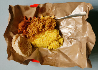close up yellow rice with chicken, noodle, and kerupuk chips on paper oil. 
