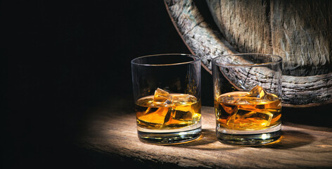Two glasses of whiskey with ice cubes in front of old barrel