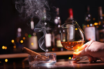 Hand with glass of whiskey or cognac and smoking cigar