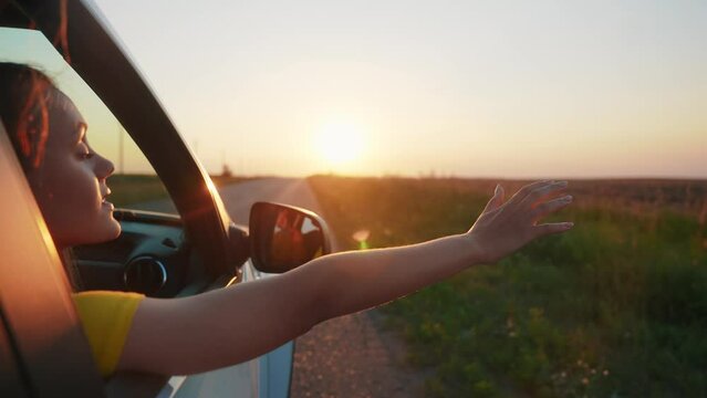 travel by car concept. the girl put her hand in the car window at sunset. freedom road a drive concept. girl travel by car goes on vacation on the road at sunset sun. summer adventure