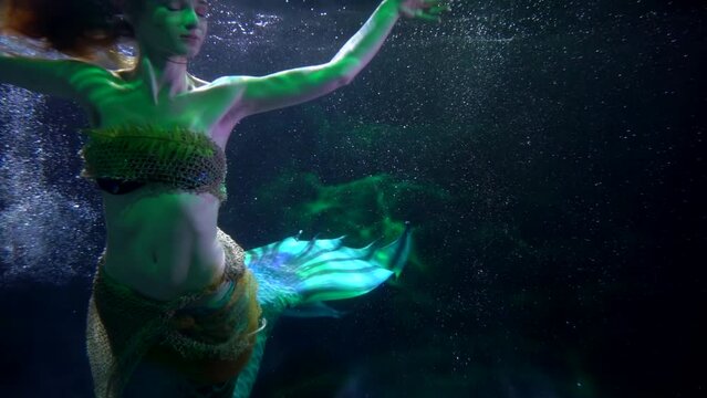 graceful mermaid with fairytale fish tail is floating in depth of sea, magical underwater shot