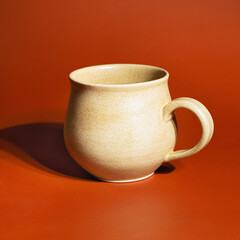 Sand-colored ceramic mug on a bright orange background. Handmade ceramics, close-up, minimalism.A coffee mug or tea cup is made of earthenware or ceramics..