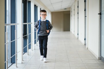 Happy cute clever boy in glasses with school bag and book in his hand. First time to school. Back to school.
