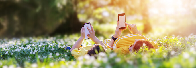 Mother and her son lying down with phones on the meadow in the park