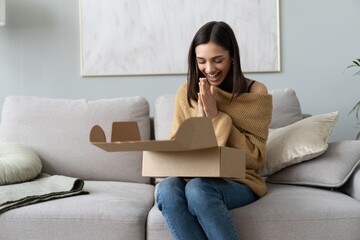Happy young woman sit on couch room unpack cardboard box buying goods on Internet. shopping online, delivery concept - obrazy, fototapety, plakaty