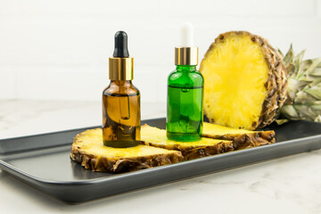 two glass bottles with a pipette with cosmetic, pineapple oil, a serum with pineapple extract for natural facial skin care. marble background,