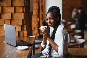 Side view of black lady enjoying morning coffee and checking emails on laptop, cafe interior, empty space