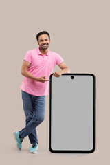 Smiling young man leaning on big smartphone and pointing with finger