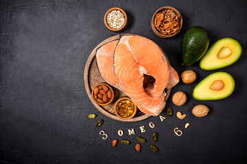 two raw salmon steaks on a round wooden tray surrounded by ripe avocado, nuts, seeds, omega3 capsules. top view. copy of the space.