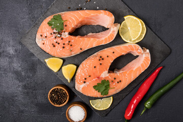 two large fresh salmon steaks on a shale board with spices. top view. black background. the concept of healthy food. omega 3.