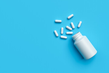 Plastic medical container and white capsule pills on blue background copy space top view. Medicine and health concept. 3d rendering.