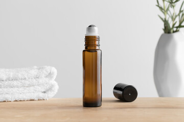 Amber glass roll-on bottle mockup with a towel and a rosemary on the wooden table.