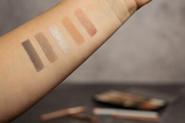 Eye shadow swatches on a hand against a marble dressing table with shadows and brushes.