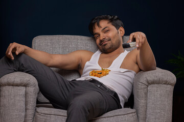 Portrait of an exhausted young man lying on sofa and watching television
