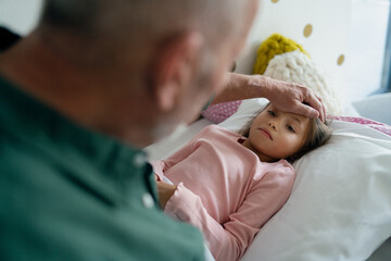 Grandfather taking care of his ill granddaughter lying in bed.