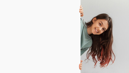 Happy Girl Hiding Behind Empty White Board Over Gray Background