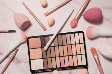 A nude eyeshadow palette and makeup artist's tools on a marble vanity. Brushes for powder, blush,...