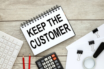 Keep the Customer. notepad with text on a wooden background near a white computer keyboard and other supplies