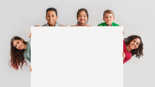 Happy Diverse Kids Hiding Behind Empty White Board, Gray Background