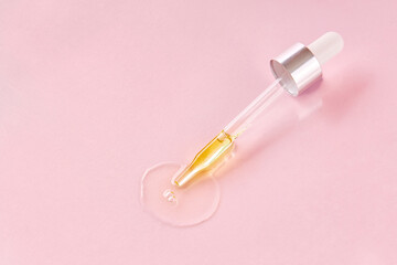 Close up of pipette with pouring liquid essential oil on pink background. Dropper with a falling drop of aromatherapy oil close-up