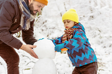 Little boy and his father having fun outdoors on the snow. They are making a snowman together.