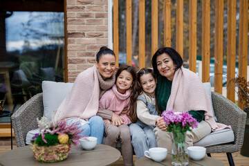 Three generations females sitting and drinking tea and looking at camera outdoors in patio in autumn