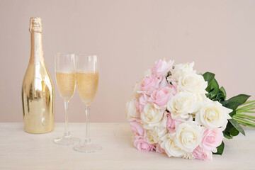 Two glasses, a golden bottle of champagne, a bouquet of roses and pink confetti on the table. Romantic date on Valentine's Day with copy space.
