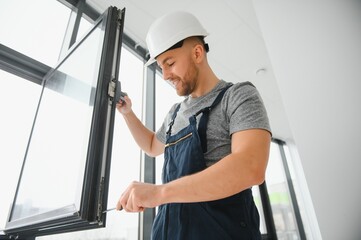 Workman in overalls installing or adjusting plastic windows in the living room at home