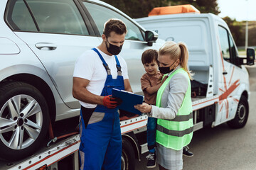 An mother with a small child talks with worker nad waits for a tow truck to take away their broken...