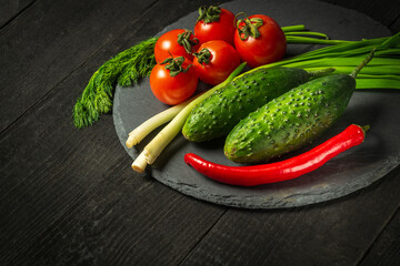Fresh vegetable salad set. Red tomatoes and green young onions with cucumber on a black plate. Vitamin breakfast or dinner