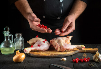 The cook prepares raw chicken legs in the kitchen. The chef puts the red viburnum on the chicken legs before baking. National dish