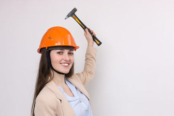 Girl engineer in an orange construction helmet with a hammer on a white background.