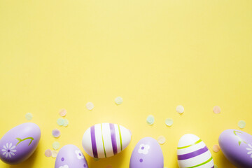 painted easter purple eggs with ornament and decor on yellow light pastel background with copy space