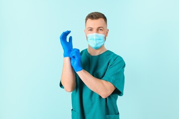 Fototapeta na wymiar Protection against coronavirus. Half photo of mature male doctor in medical uniform putting on protective sterile blue gloves while standing against blue background. Healthcare. Coronavirus, Covid-19