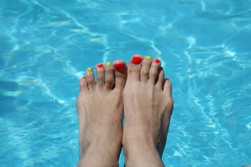 legs of a girl with a pedicure on the background of blue water in the pool