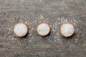 A wooden bowl of salt crystals on a wooden background. Salt in rustic bowls, top view with copy...